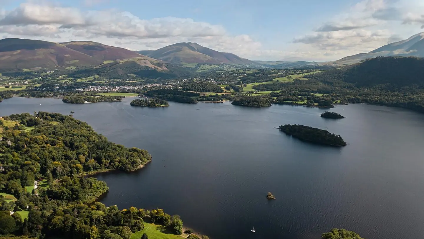 A Lake District valley from the air, with a long lake, wooded islands and fells behind.