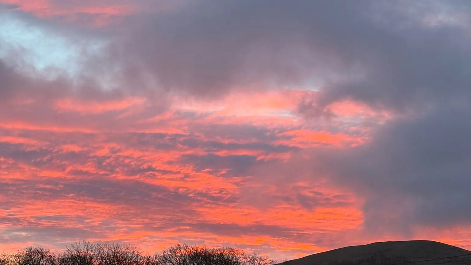 A deep pink and red sunset over the fell behind the holiday park at Lamplugh, with the caravans lit from inside.