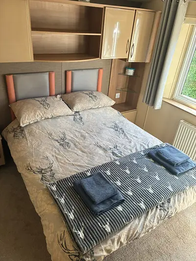 The double bedroom in The Lake District Caravan with an orange trimmed headboard and folded towels.