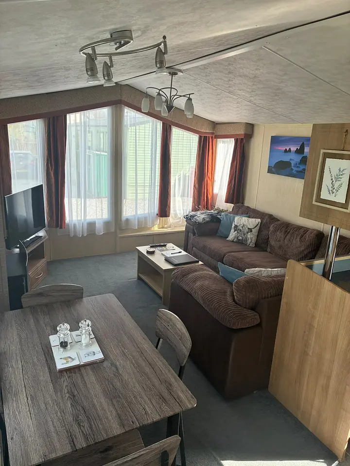 The lounge and dining area in The Lake District Caravan, with a large brown corner sofa and blue cushions.