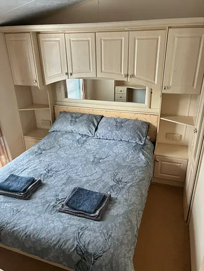 The double bedroom in The West Lakes Caravan with overhead lockers, a mirrored wardrobe and towels folded on the bed.