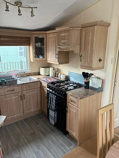 The kitchen in The West Lakes Caravan with light wood units, a gas cooker and a kettle.