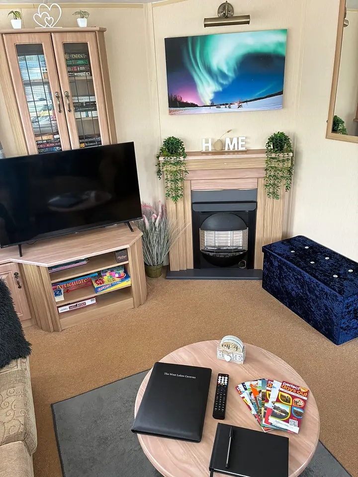 The lounge in The West Lakes Caravan, with an electric fire, a framed aurora print above it and board games stacked by the television.